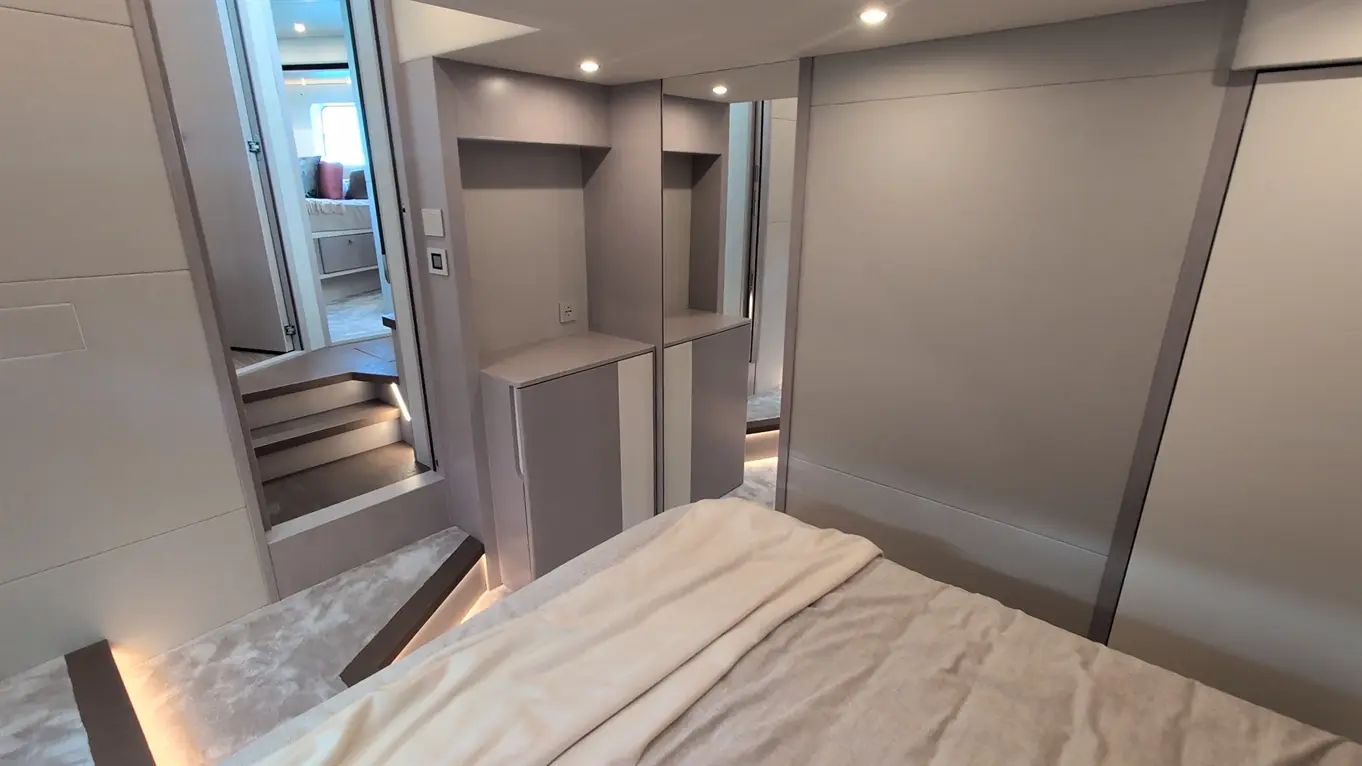 Interior of a modern bedroom featuring a bed with a white blanket, stylish storage units, and steps leading to another room.